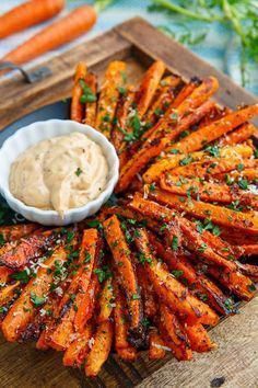 grilled carrots are arranged on a wooden platter with dipping sauce