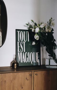 a vase with flowers on top of a wooden dresser next to a sign that says tour est magique