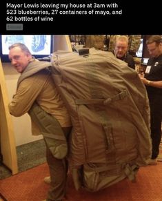 two men are standing in front of a large bag that looks like an army backpack