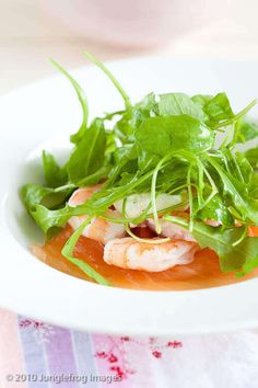 a white plate topped with salad and shrimp on top of lettuce covered in sauce