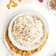 a bowl filled with white frosting surrounded by crackers and sprinkles