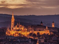 the city is lit up at night with lights shining on it's buildings and spires