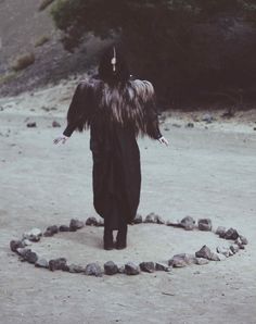 a person in a black outfit walking through a circle of rocks with their arms spread out