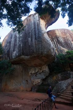 a man standing in front of a large rock formation with stairs leading up to it