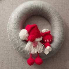 a red and white knitted santa claus decoration on top of a gray wreath with two small pom poms