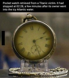 an antique pocket watch sitting on top of a glass stand with a chain around it