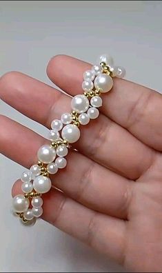 a hand holding a gold and white bracelet with pearls on it's end,