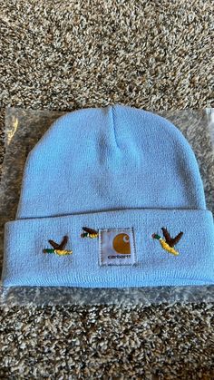 a blue beanie with two birds on it sitting on the ground next to a package