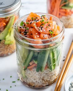 a jar filled with rice, carrots and cucumbers next to chopsticks