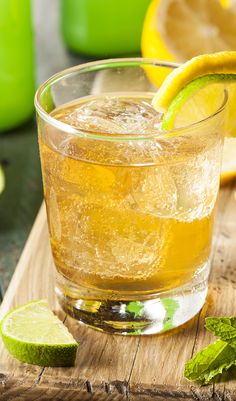 a close up of a drink on a wooden table with limes and lemon slices