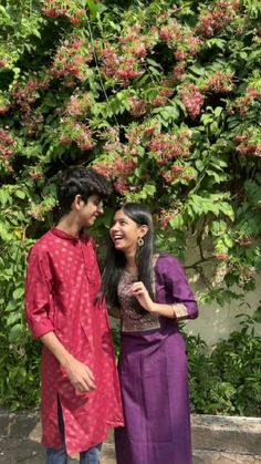 a man and woman standing next to each other in front of a tree with pink flowers