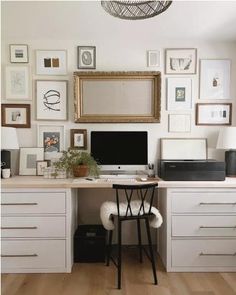 a home office with white drawers and lots of framed pictures on the wall above it