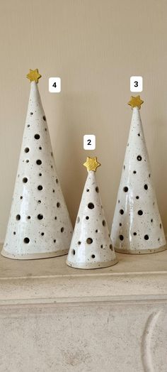 three white ceramic christmas trees with gold stars and numbers on them, sitting on a mantle