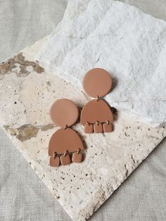 two brown earrings sitting on top of a stone slab