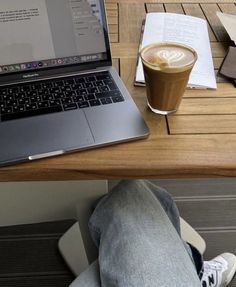 a laptop computer sitting on top of a wooden desk next to a cup of coffee