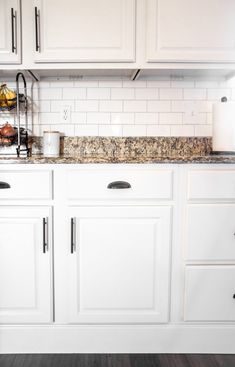 a kitchen with white cabinets and marble counter tops