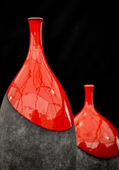 two red vases sitting on top of some gray rocks and one is in the shape of a cone