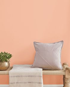 a wooden bench topped with a pillow next to a potted plant and a blanket