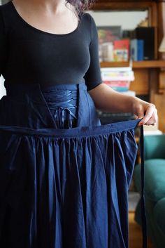 a woman in a black top is wearing a blue skirt and holding a pair of scissors