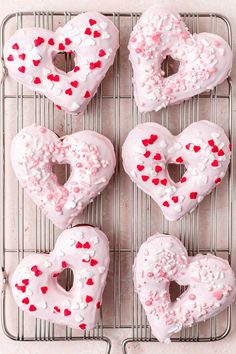 heart shaped doughnuts on a cooling rack with sprinkles and hearts