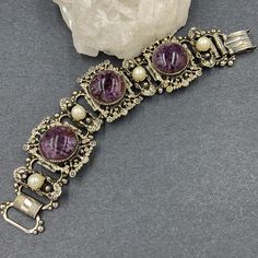 Vintage Victorian Revival Book Chain Bracelet With A Wonderful “Old Gold” Plating. The Large Purple Glass Cabochons Show A Mottled Effect And Are Mounted On Large Ornate Panels. Smaller Elongated Panels Are Adorned With Glowing Faux Pearls. Tight And Secure Fold Over Clasp. Measures 7 By 1 1/4” And Is Unsigned. Vintage Purple Metal Bracelets, Vintage Purple Bracelet For Formal Occasions, Purple Nickel-free Jewelry For Formal Occasions, Vintage Amethyst Bracelet Jewelry, Elegant Nickel-free Purple Bracelets, Elegant Nickel Free Purple Bracelets, Handmade Vintage Purple Bracelets, Adjustable Purple Bracelets For Formal Occasions, Formal Adjustable Purple Bracelets