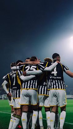 a group of soccer players huddle together in the middle of a field at night