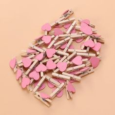 a pile of wooden clothes pins with pink hearts on them, against a beige background