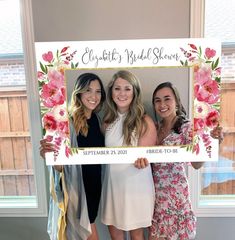 three women pose for a photo in front of a floral frame that says, elizabeth's bridal shower