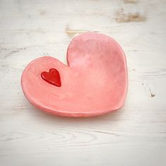 a pink heart shaped dish sitting on top of a white wooden table with a red heart in the center