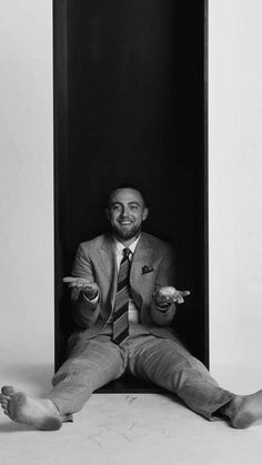 a man in a suit and tie sitting on the floor with his hands out while holding something