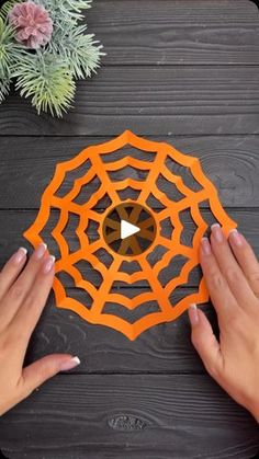 two hands are holding an orange paper spider web on a wooden table with succulents