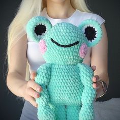 a woman is holding a crocheted frog stuffed animal