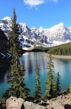 the mountains are covered in snow and there is a blue lake surrounded by pine trees