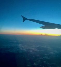 the wing of an airplane as it flies in the sky over clouds at sunset or dawn