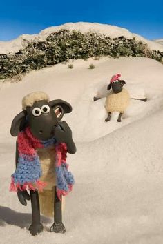 two sheep are standing in the snow with one looking at the camera while another looks on