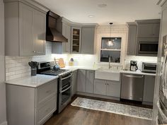 a kitchen with gray cabinets and white counter tops, stainless steel appliances and wood flooring