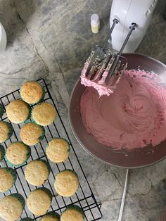 cupcakes are being frosted with pink icing next to a cooling rack