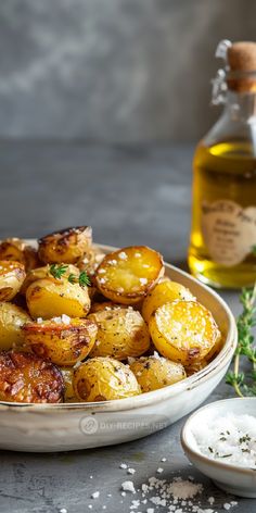 a bowl filled with cooked potatoes next to a bottle of olive oil and sprigs of parsley