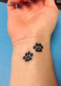 a woman's wrist tattoo with two paw prints on the left side of her arm