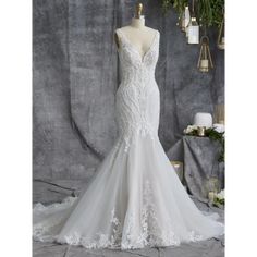 a white wedding dress on display in front of a gray backdrop with candles and greenery