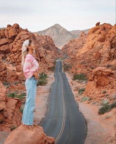 a woman standing on top of a rock next to a long road in the desert