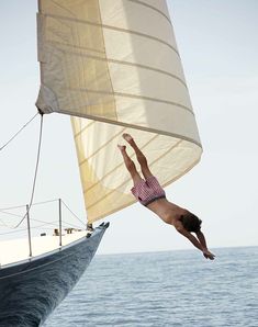 a person jumping off the side of a boat into the water with a sailboat in the background