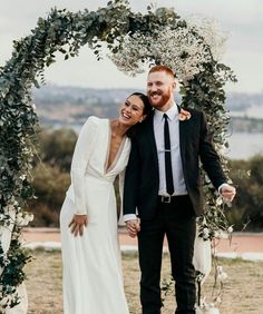 a newly married couple standing under an arch with greenery and white flowers on it