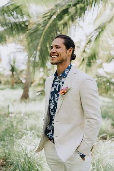 a man in a white suit and flowered shirt smiles while standing in the grass