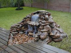 there is a small waterfall made out of rocks and wood in the yard with water coming from it