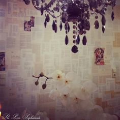 a chandelier hanging from the ceiling in front of a wall covered with newspaper