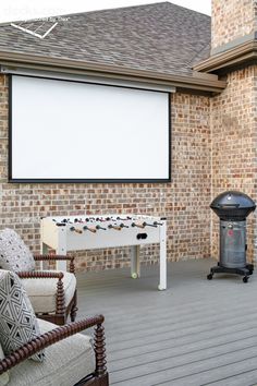 a large screen on the side of a brick building with chairs and a foo - ball table