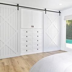 a bedroom with white walls and sliding doors on the wall, along with hardwood flooring