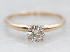 a yellow gold engagement ring with a round cut diamond in the center, on a white background