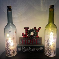 two wine bottles with christmas lights in them on a table next to a sign that says joy hope believe